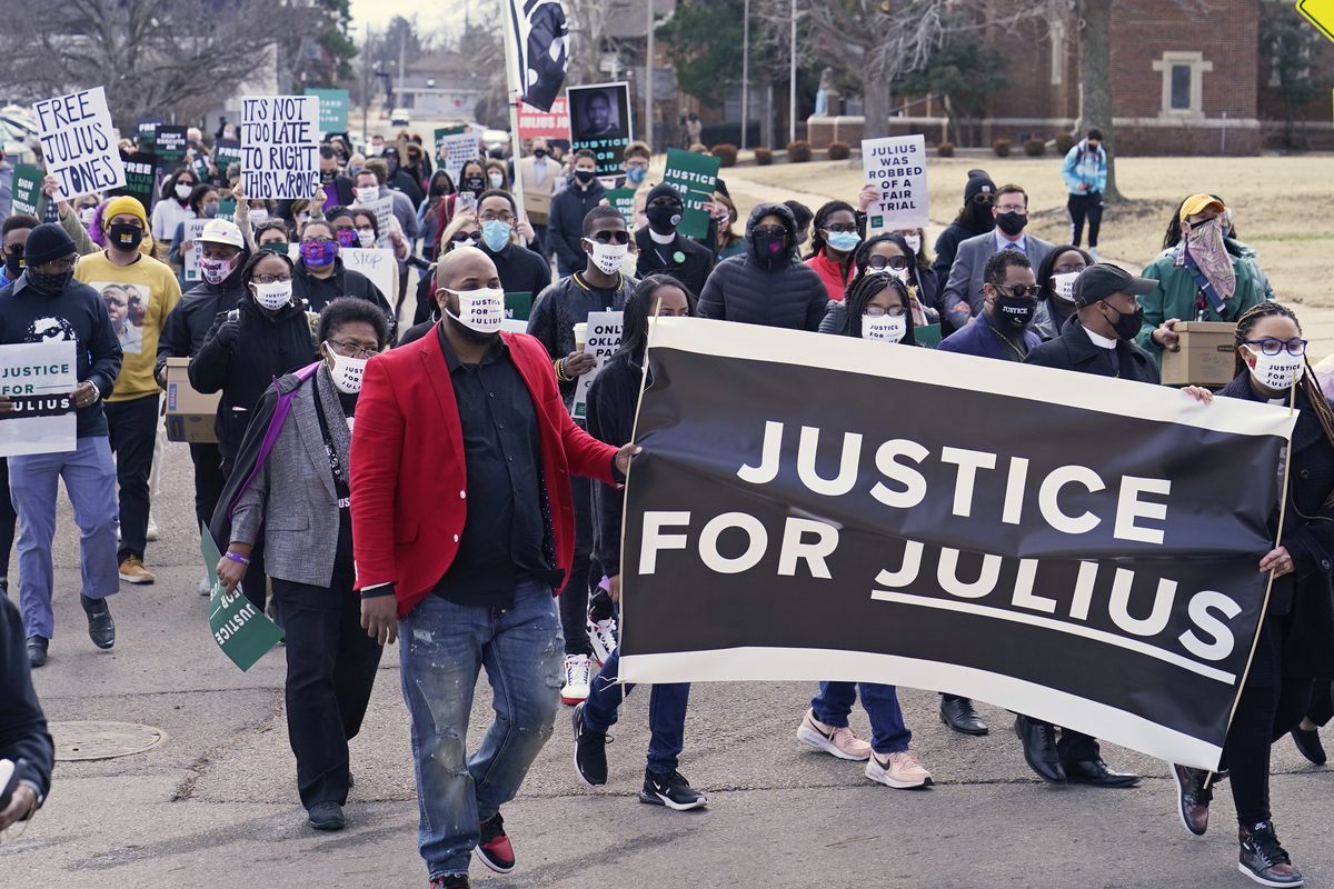 Protesters march down a city street carrying a banner that reads “Justice for Julius.”