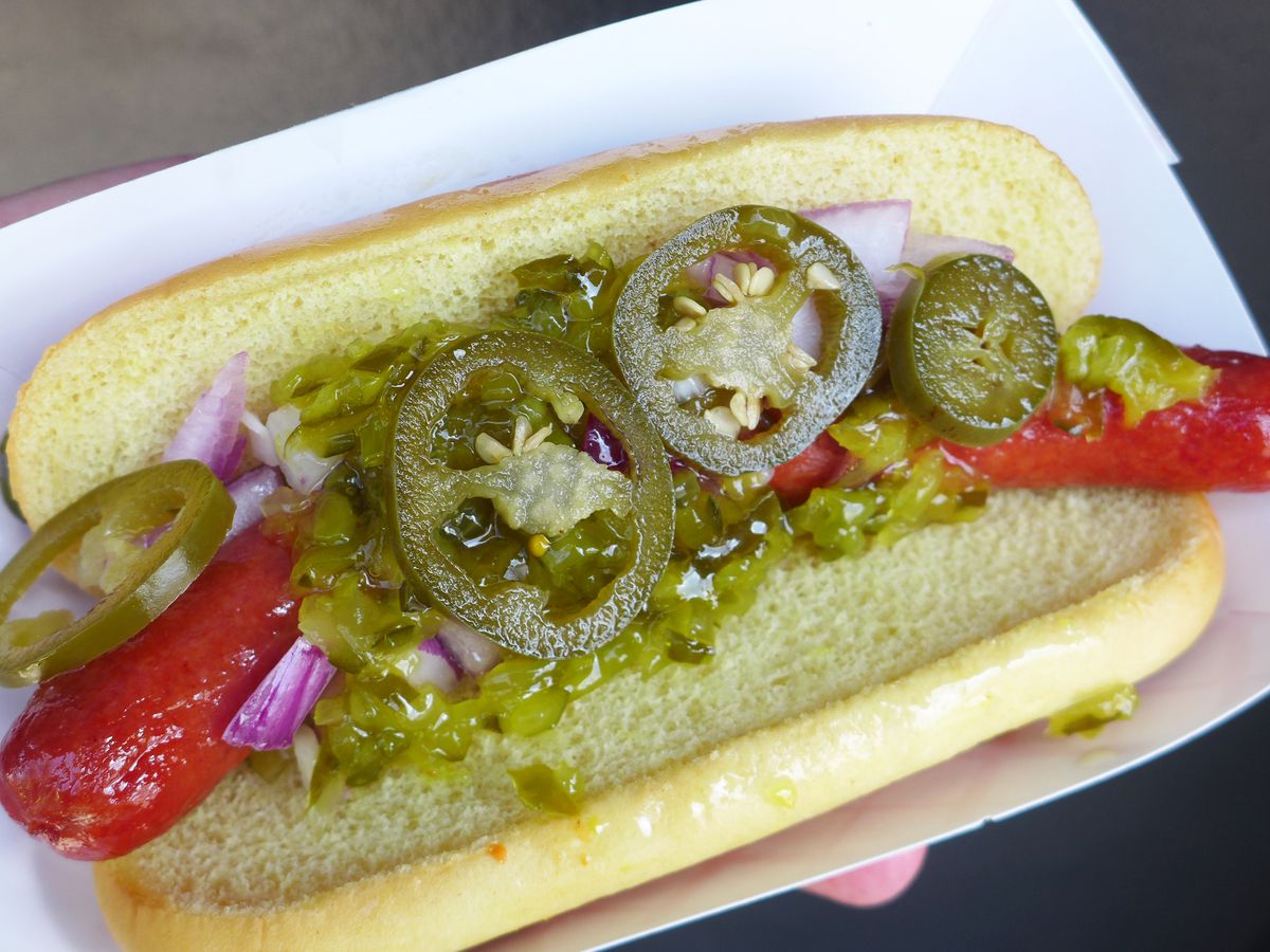 A glistening hot dog in a bun with pickled jalapenos and green sweet relish.