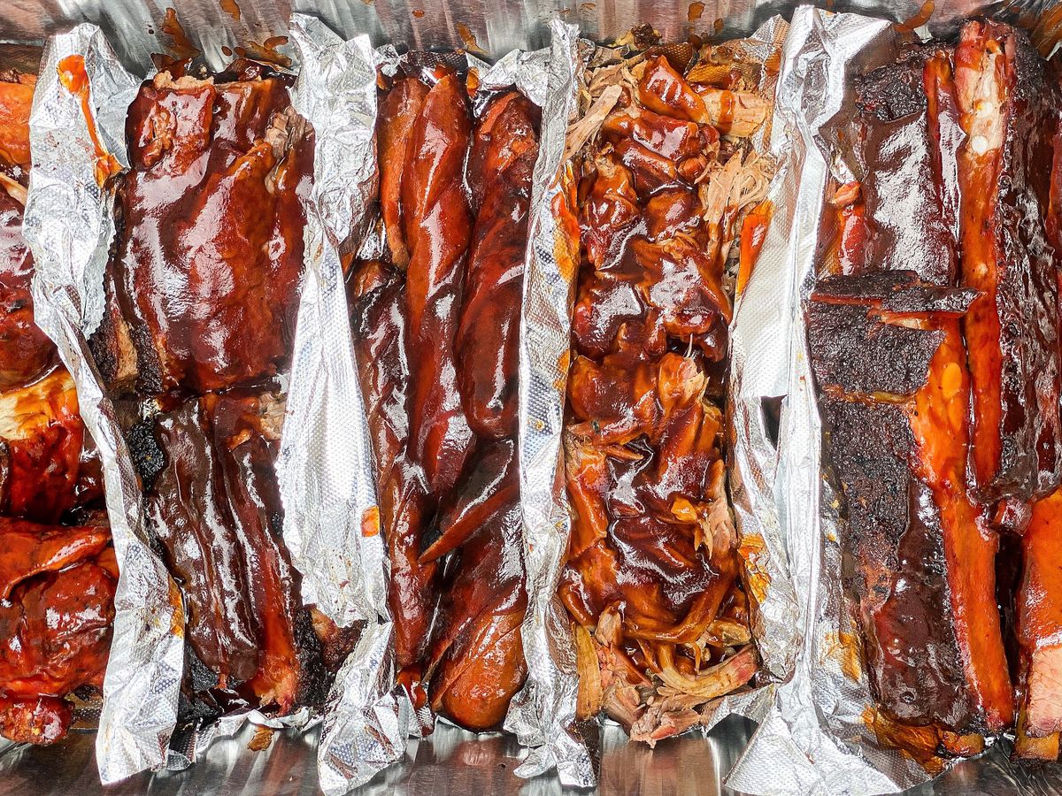An overhead shot of saucy meat from a barbecue restaurant, including very bark-heavy ribs from the Woods restaurant.