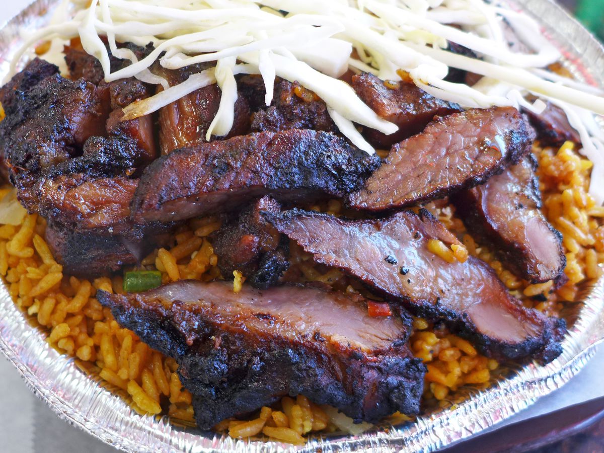 A carryout tin of orange rice topped with jerk pork and shredded cabbage.