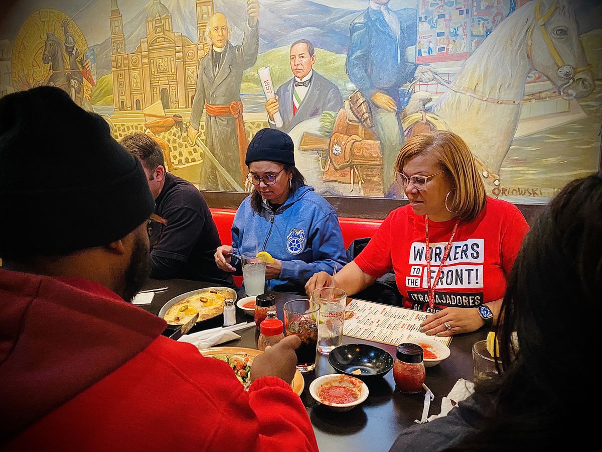 Center left, Veronica Sawyer, of Teamsters Local 1038, wearing a blue Teamsters jacket, and Nia Winston, president of UNITE HERE Local 24, wearing a red T-shirt, taking a lunch break at Mexican Village Restaurant in Detroit’s Hubbard Richard neighborhood on October 18, 2023, day 2 of the casino workers strike.