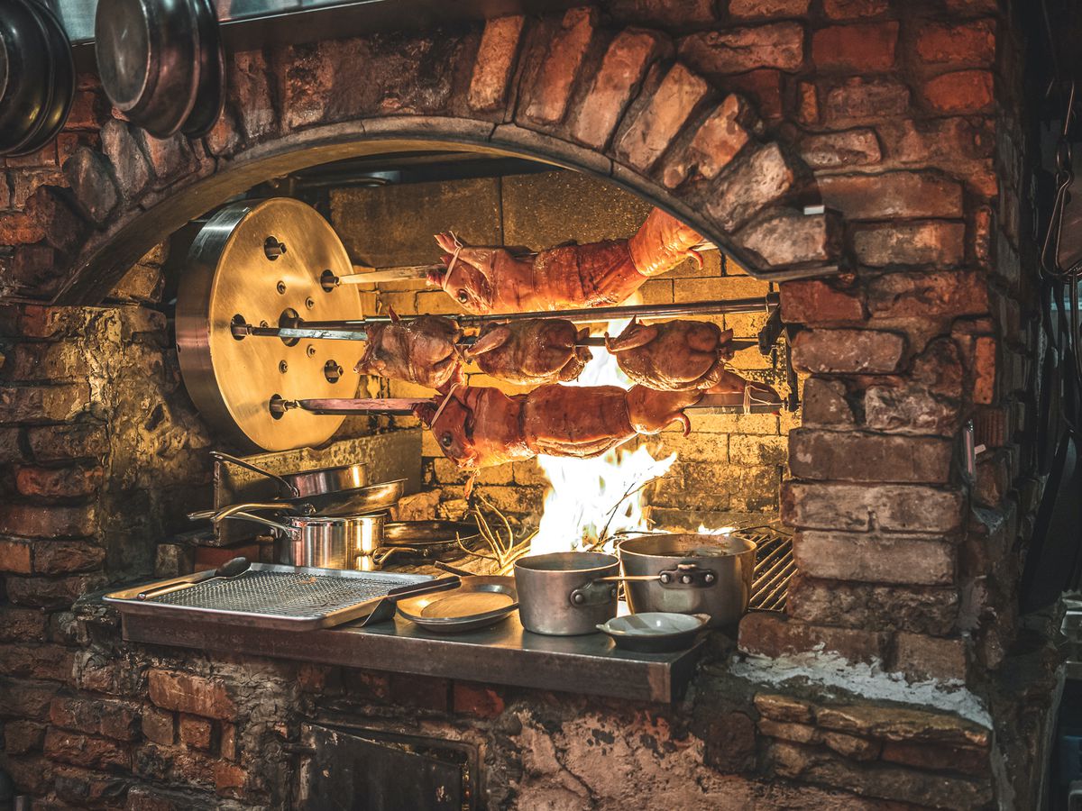 A brick lined oven with wood fire with pigs on a spit roast.