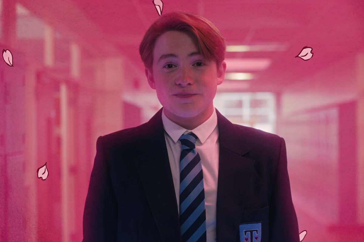Heartstopper's lead walks down the school hallway in their uniform, set against a pink background