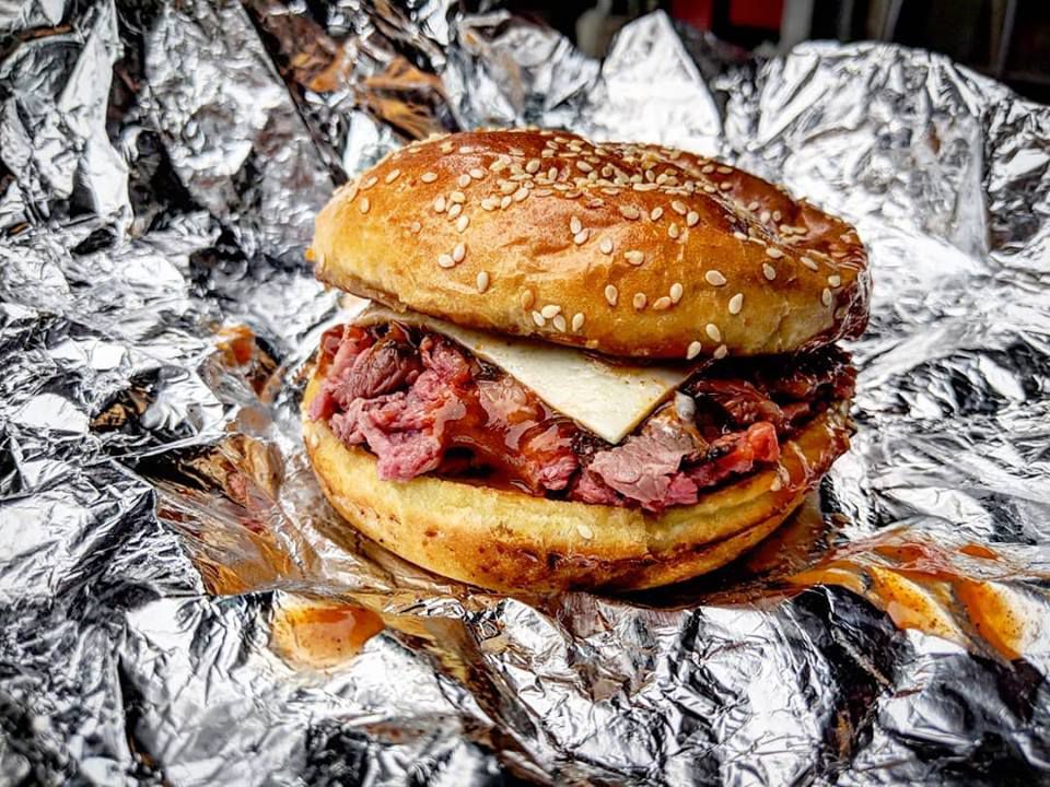 A three-way junior roast beef sandwich on a sesame bun sits on aluminum foil