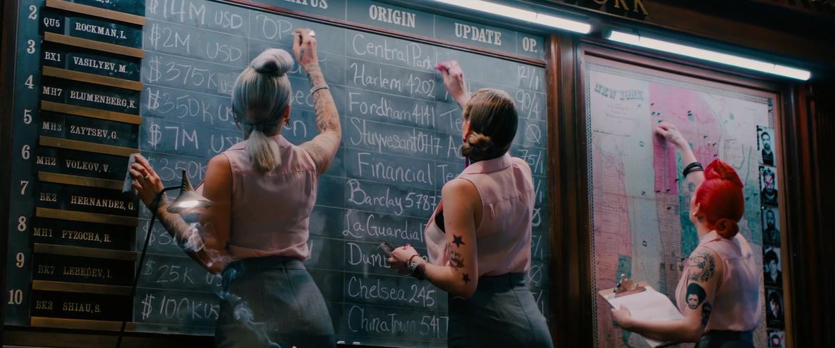 three tattooed women update a chalkboard with bounties at the assassin’s guild or whatever in John Wick: Chapter 2