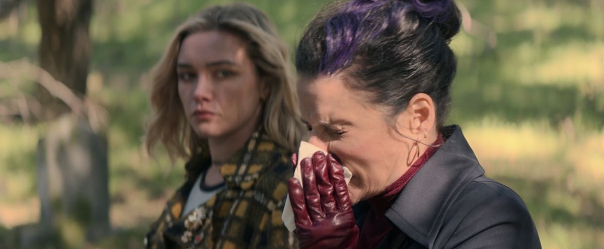 Valentina Allegra de Fontaine (Julia Louis-Dreyfus) blows her nose at Black Widow’s gravesite as Yelena Belova (Florence Pugh) looks on, annoyed in Black Widow.