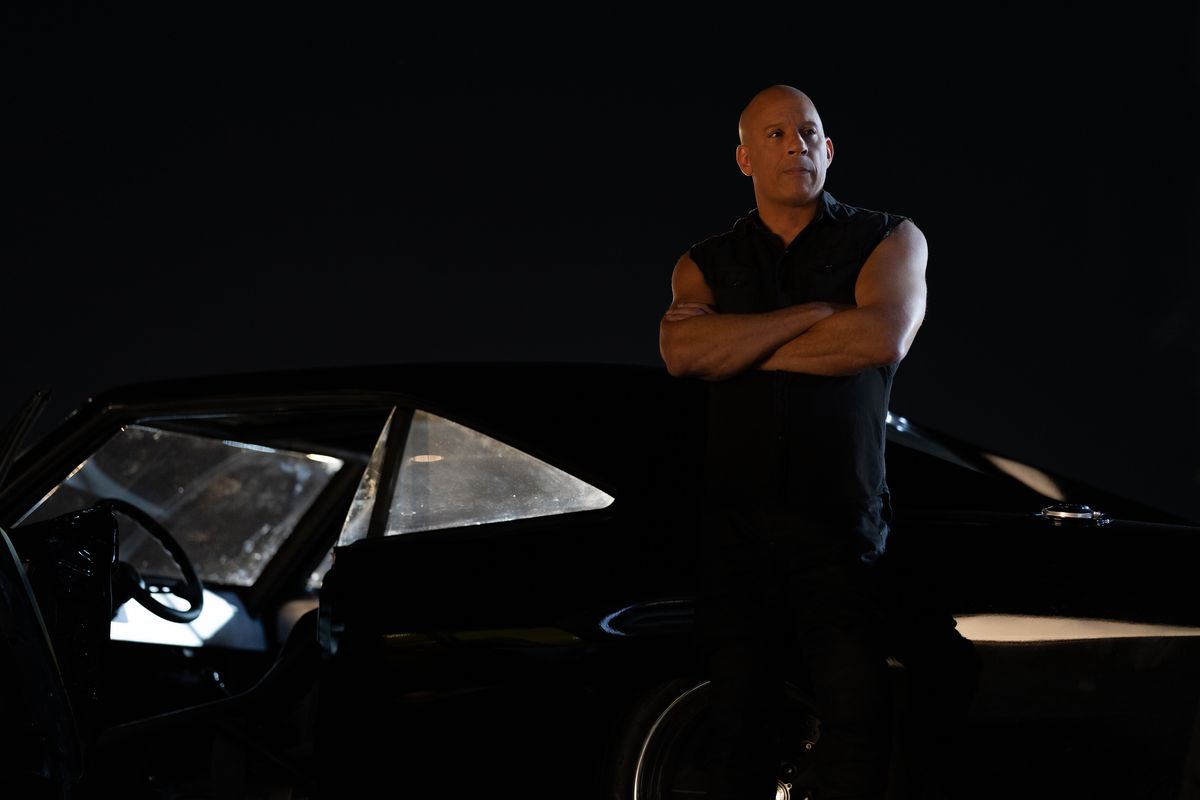 Vin Diesel, arms crossed, leaning with his back to a car.