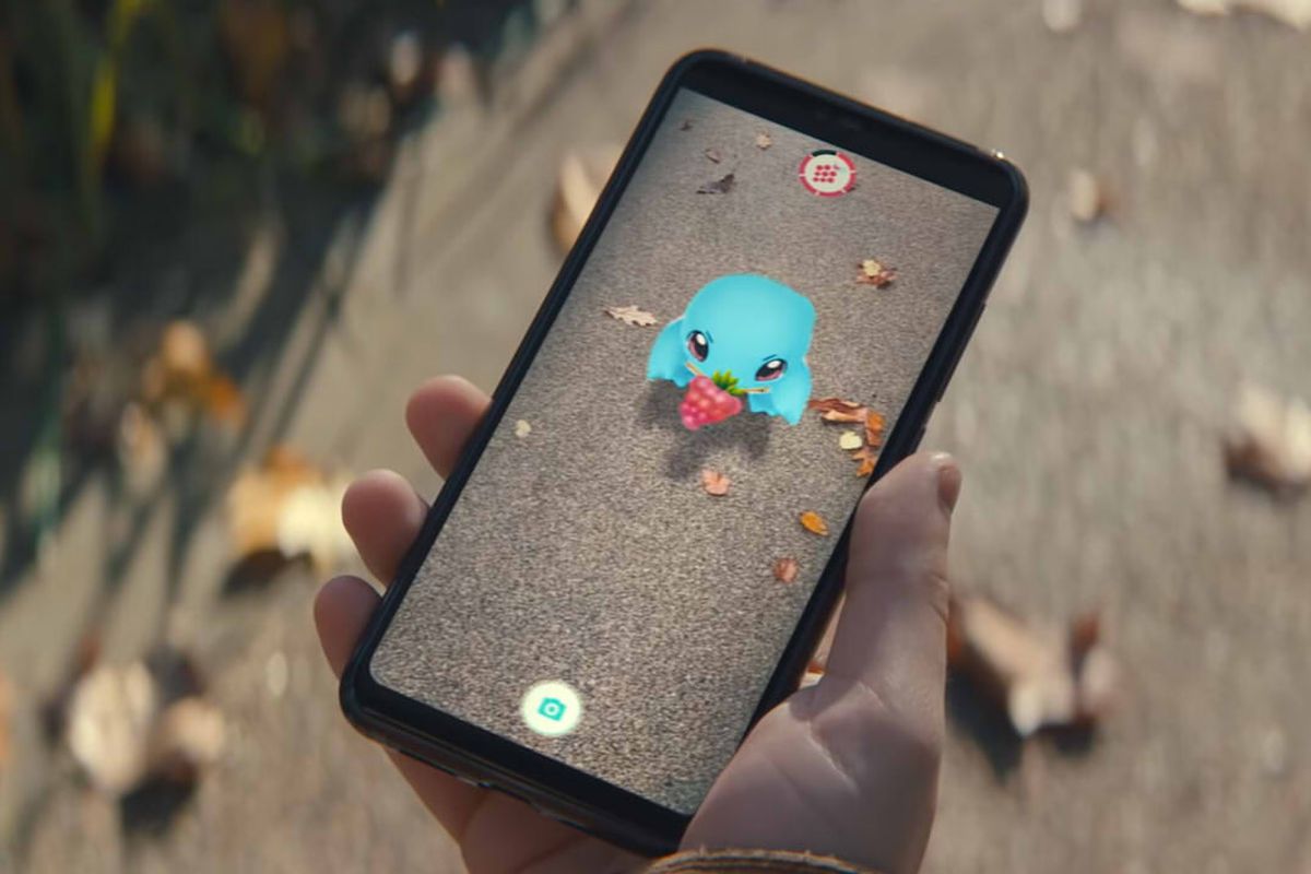 A hand holds up a phone, that has a Squirtle eating a berry on it