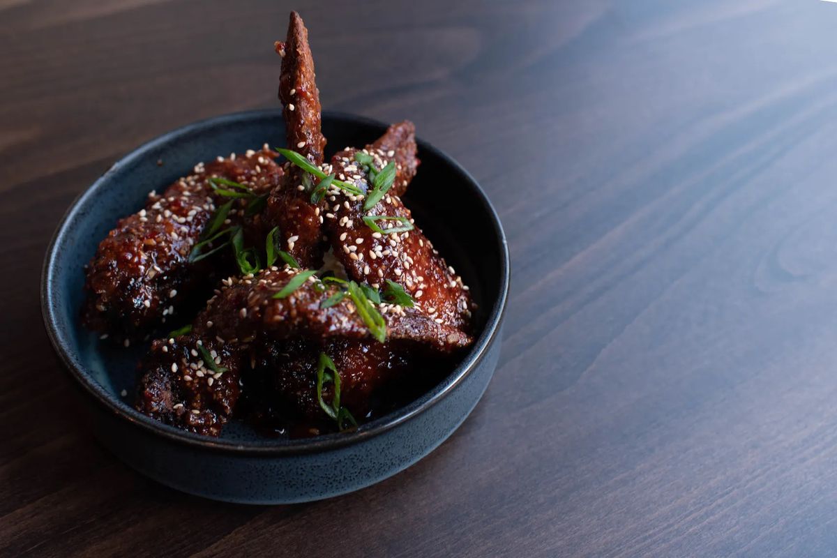A bowl of chicken wings topped with scallions and sesame seeds.