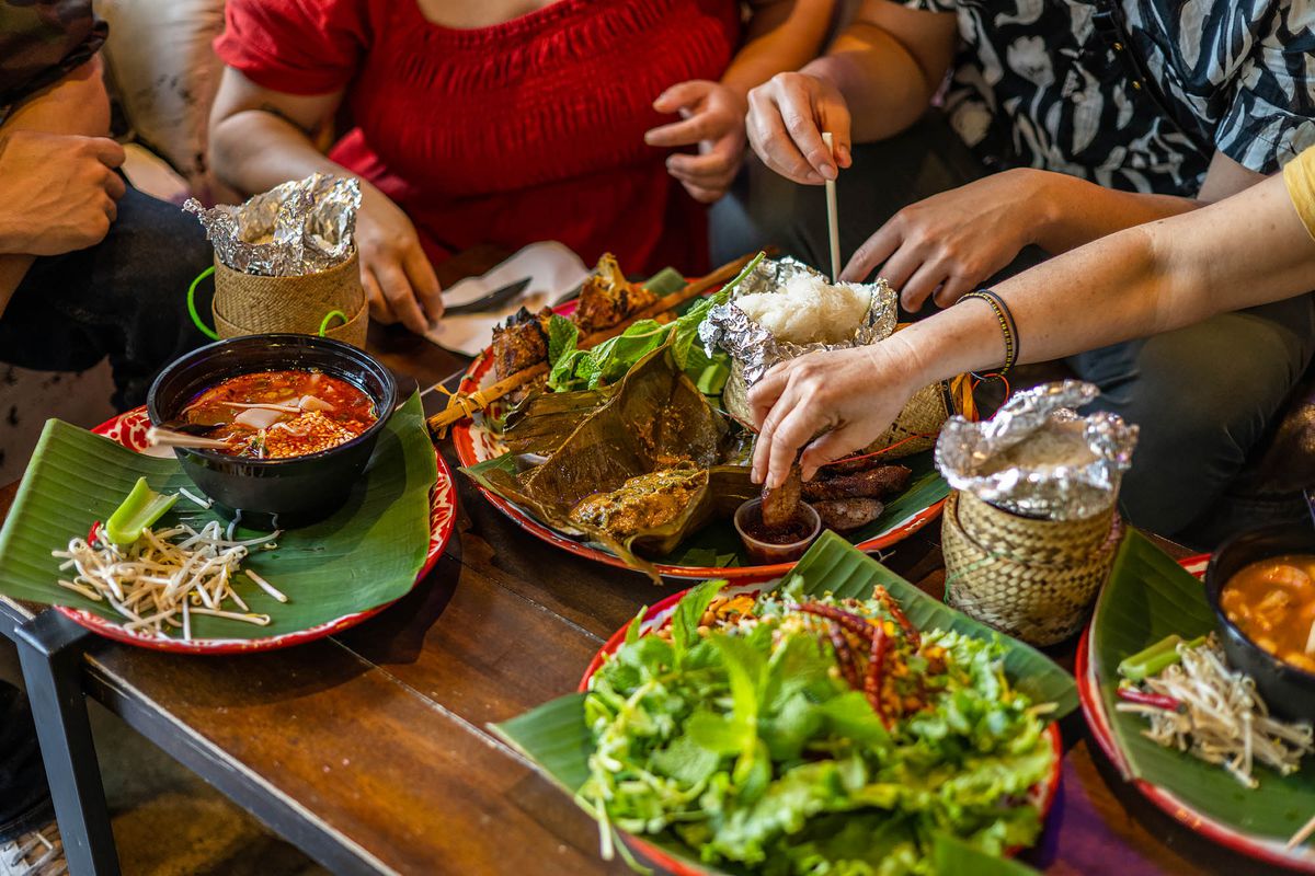 Diners dig into a selection of Laos foods served on a low wooden table.