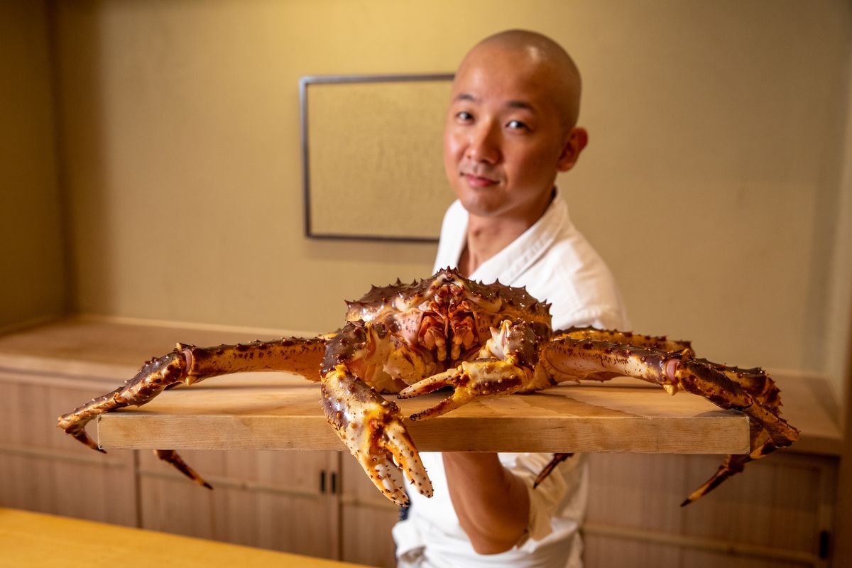 Chef Nozomu Abe stands behind the sushi bar with a giant live king crab.