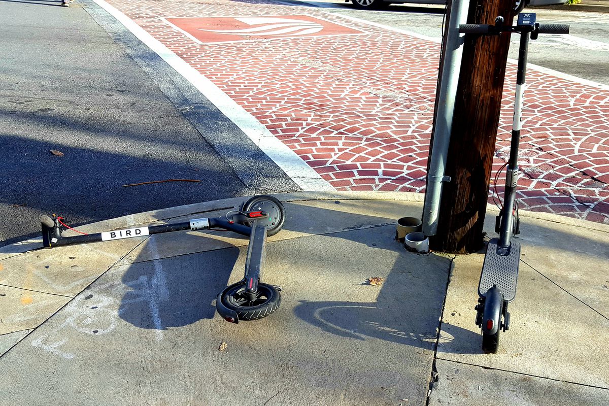 A picture of two Bird e-scooters parked on a sidewalk, one knocked over on its side.
