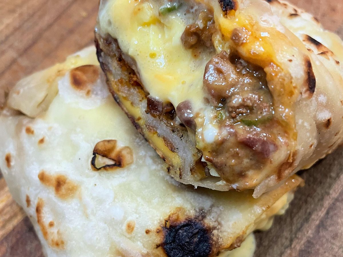 A burrito is cut in half with one side revealed oozy yellow eggs, meat, and cheese.