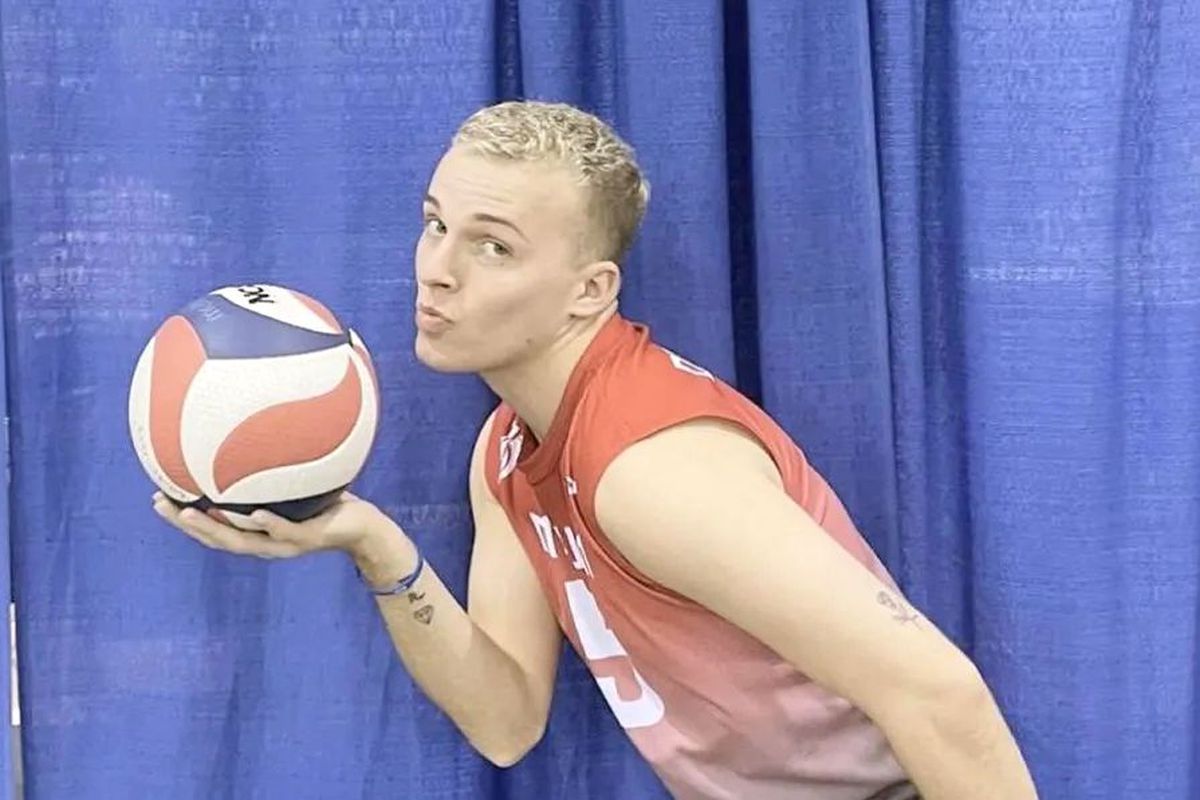 A volleyball player poses with a volleyball while smiling