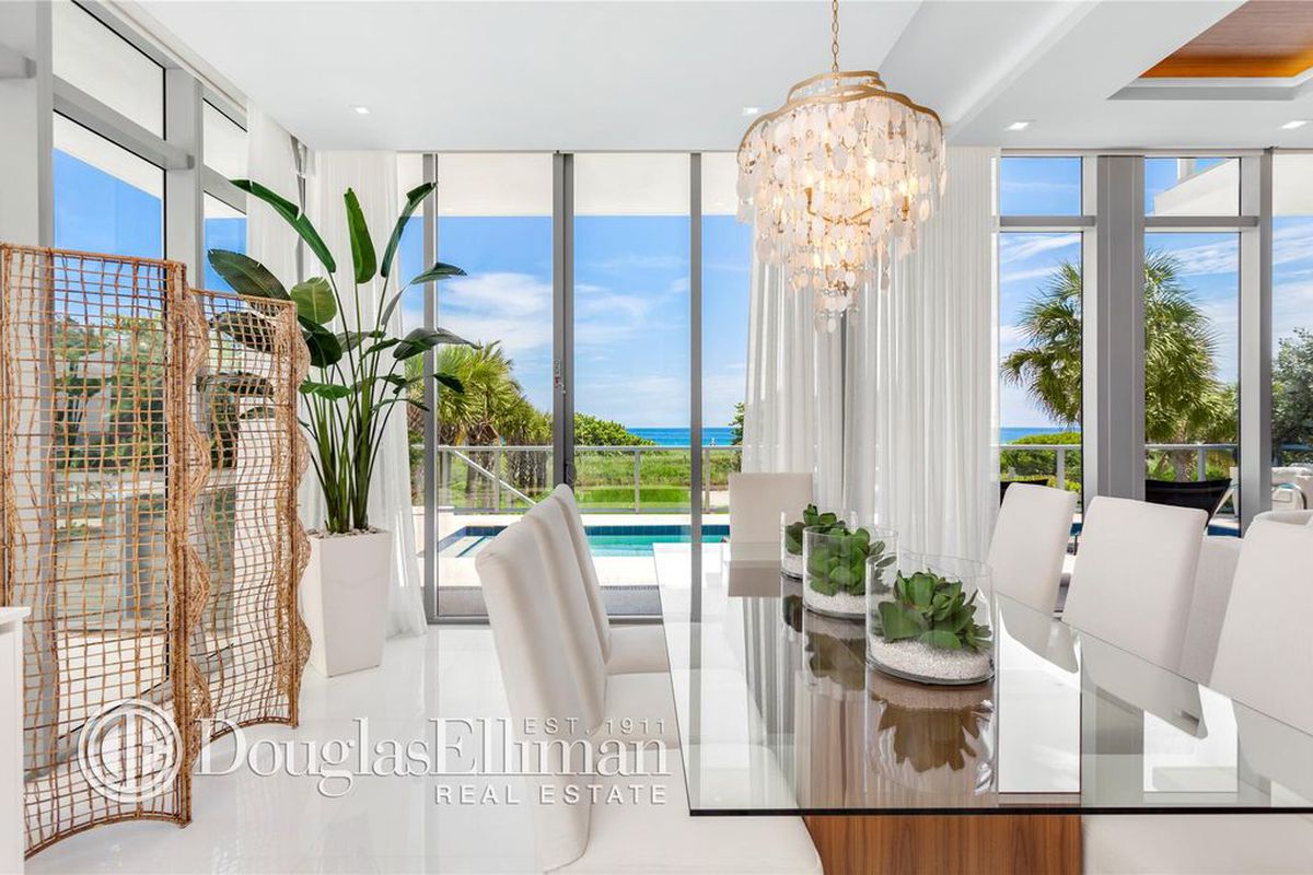Inside the dining area of a oceanfront townhome in Surfside with  white walls and floors, and a glass table