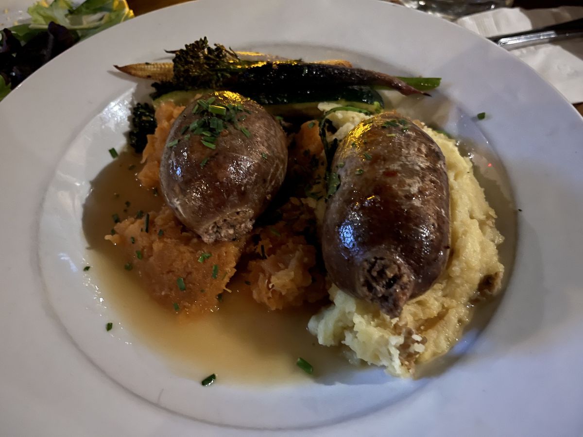 A white plate with two pieces of haggis laid on mashed potatoes and parsnips.