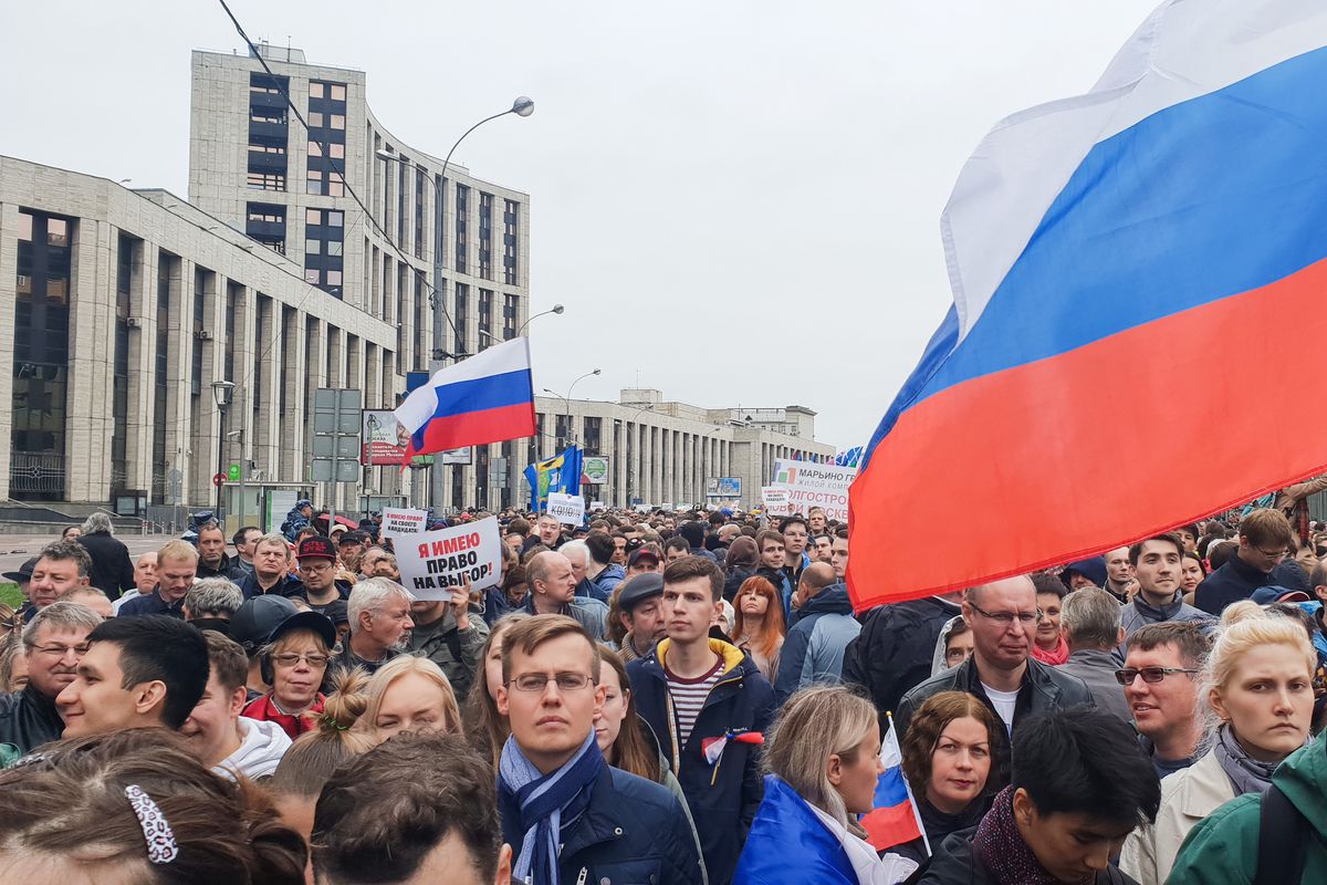 A crowd fills a street in Moscow as people carry flags in protest.