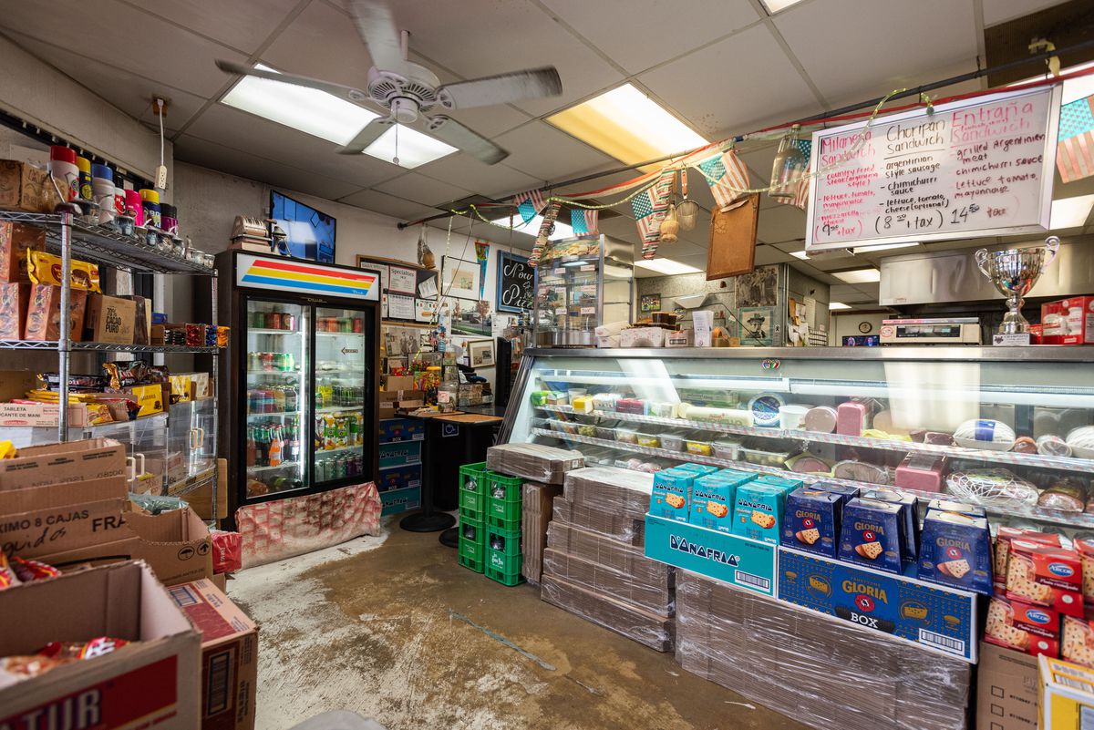 A side shot of a cluttered restaurant deli space with hanging signs and lots of stacked items.