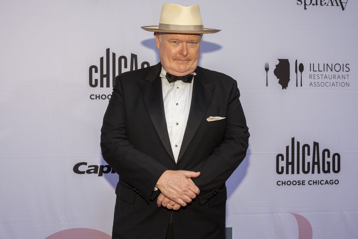 A man in a tuxedo and white hat poses on the red carpet.