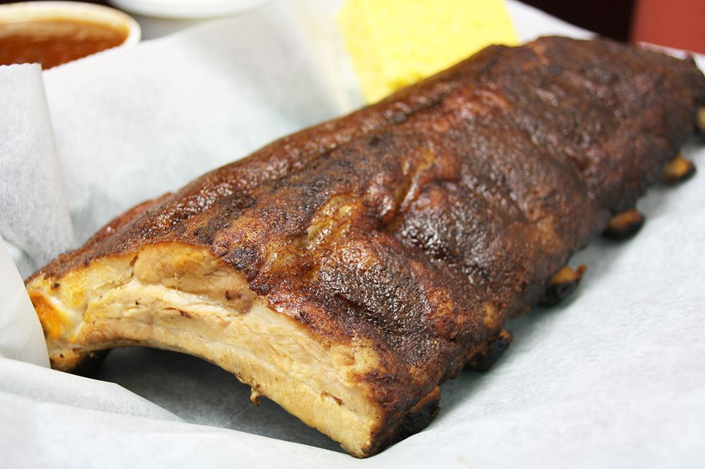 A rack of dry-rub ribs sits on white paper with a small cup of barbecue sauce visible in the background.