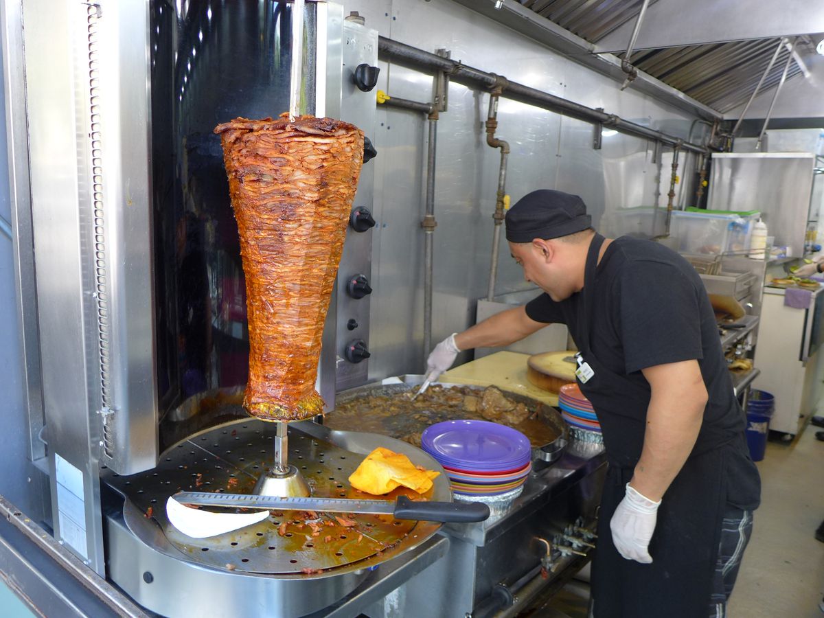 A man saws away at the al pastor meat cylinder