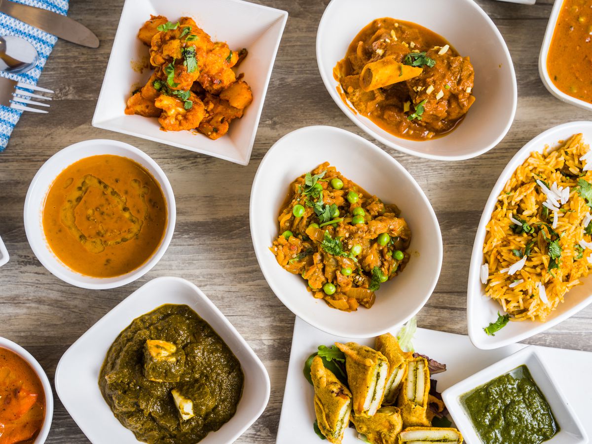 A variety of curries and other dishes from Veeray da Dhaba in NYC. The dishes are on glass plates or in glass bowls, on a wooden table. 