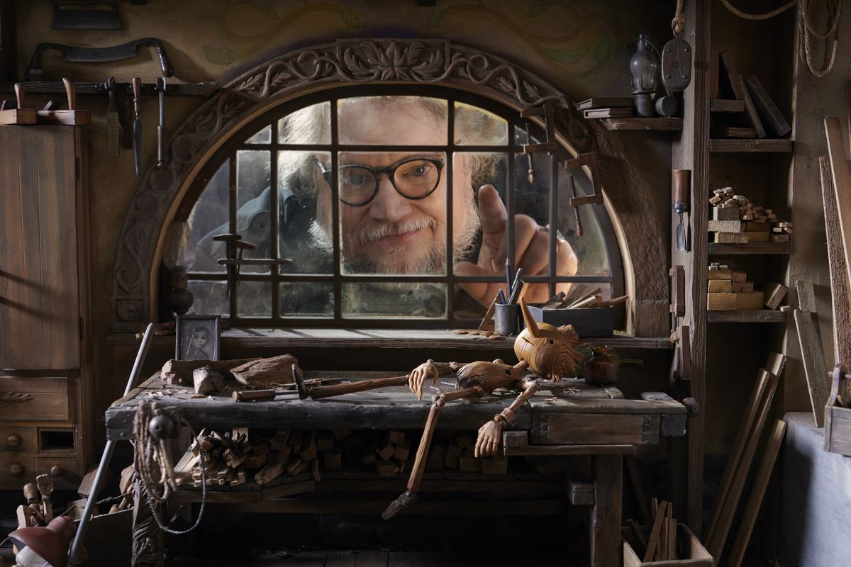 Guillermo del Toro peers through a window on the set of Pinocchio, looking like a giant
