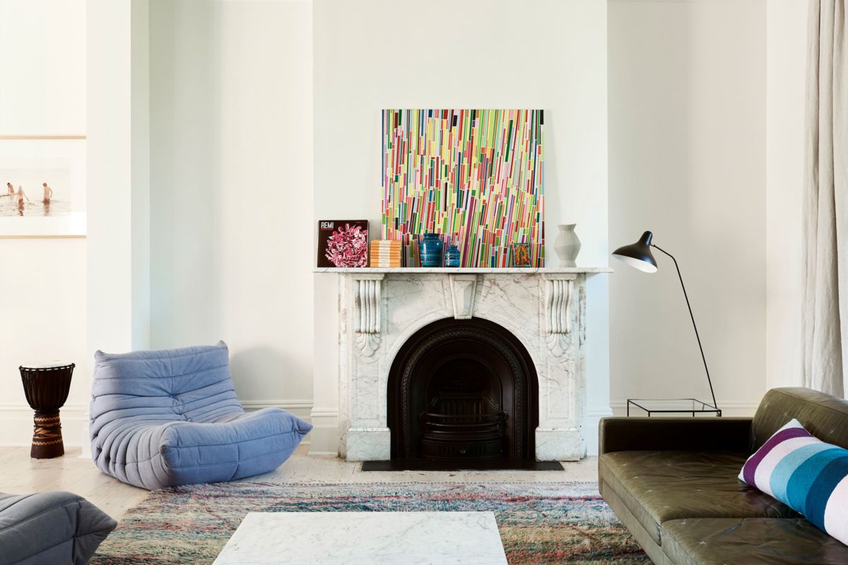Interior shot of bright white living room facing marble fireplace mantel. Modern furniture and artwork makes up the decor. 