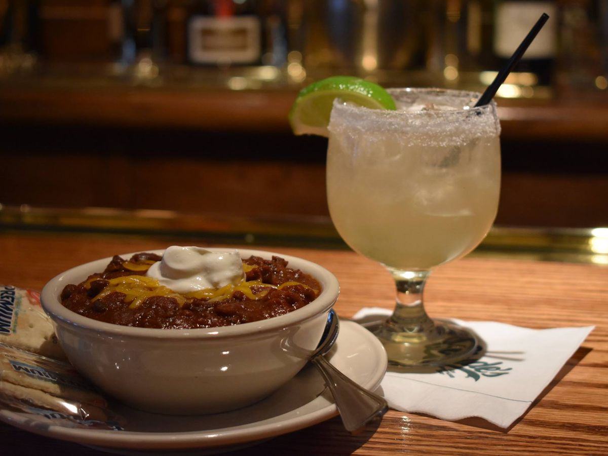 A bowl of chili with a pack of saltines to the left and a margarita with a straw to the right.