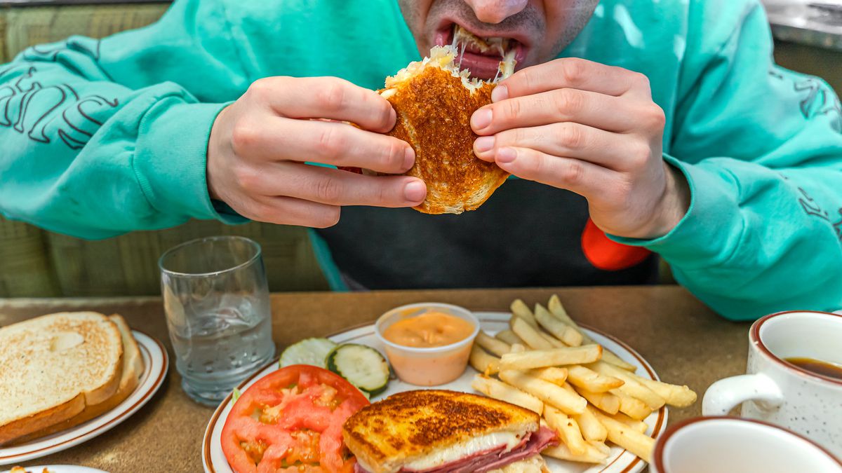 A person chomping down on a sandwich with a plate and fries.