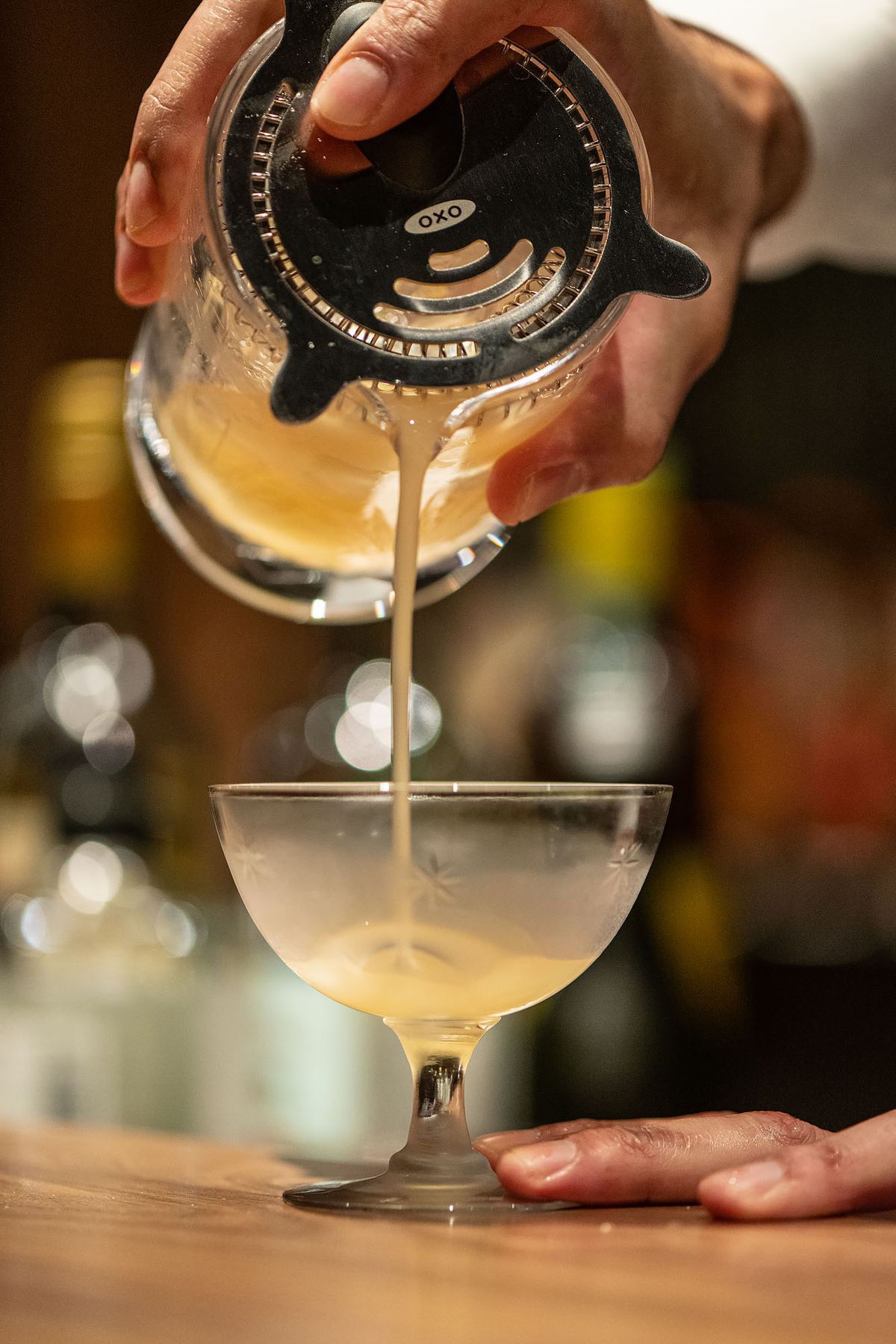 Bartender pours cocktail into a pre-chilled crystal glass.