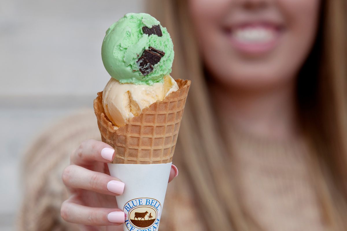 A cone with mint and vanilla ice cream held out in a hand.