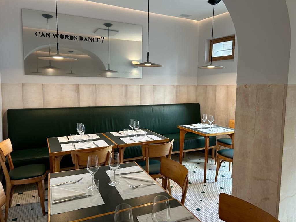A restaurant interior with sage green banquettes, wooden midcentury chairs, and tiled floors.