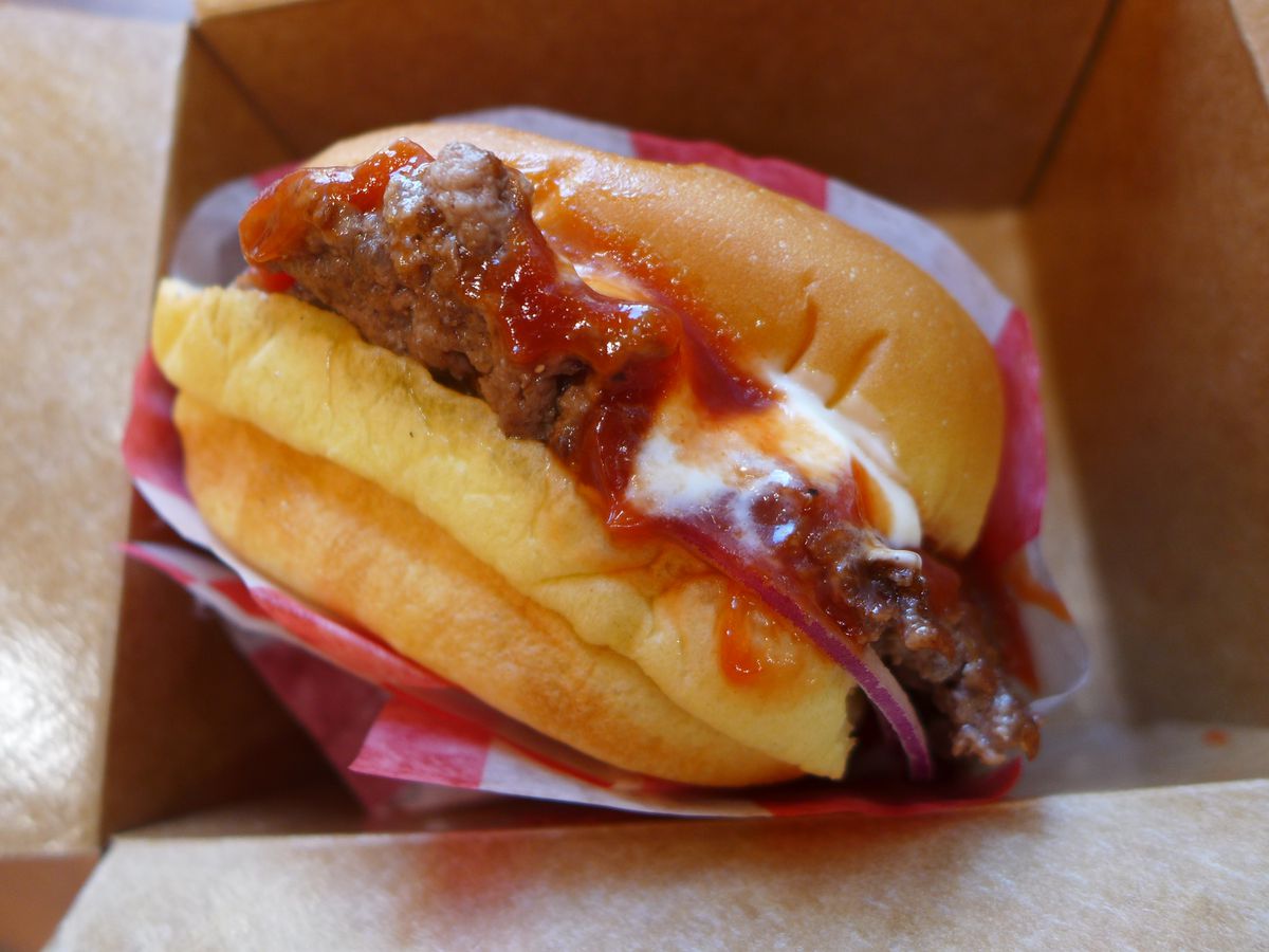 A single patty burger with an excess amount of ketchup and mayo, seen from the top of its box.