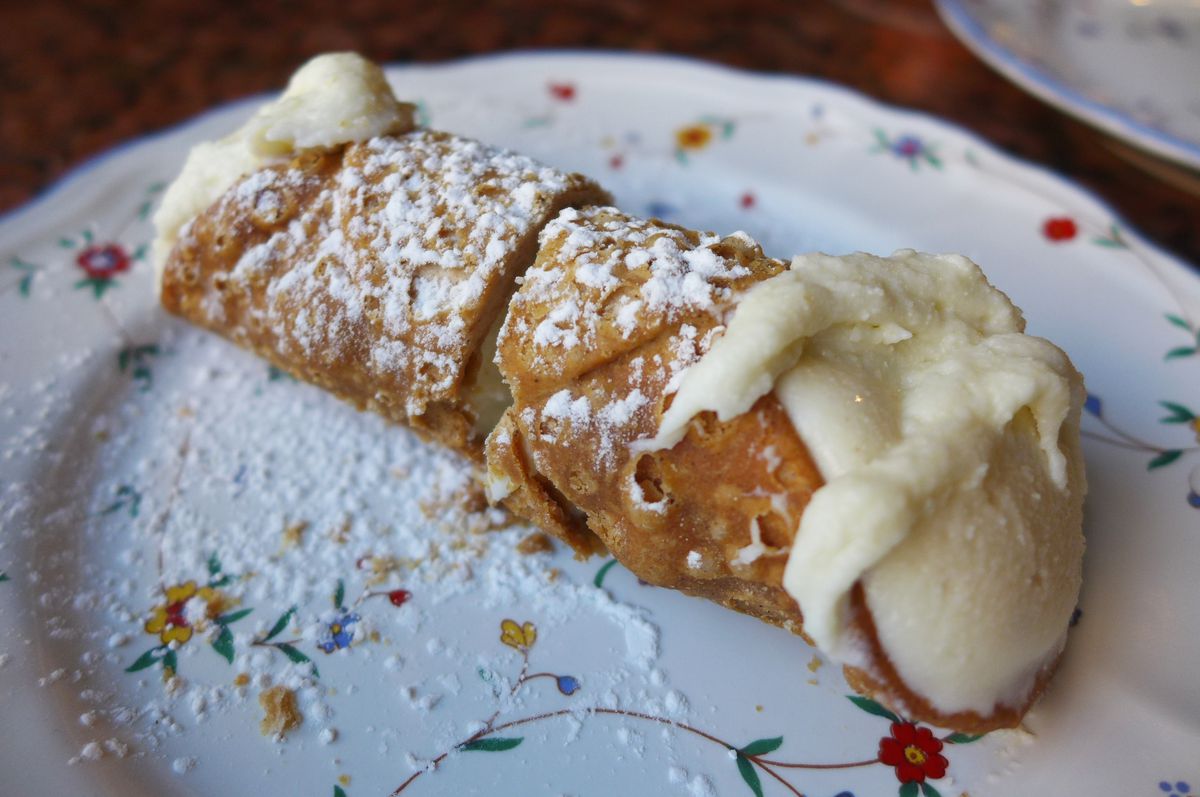A round pastry shell with white stuffing coming out both ends and powdered sugar sprinkled overall.
