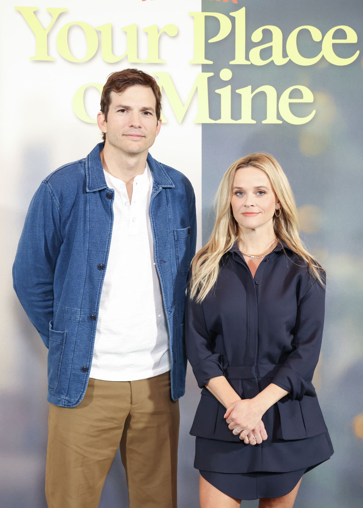 Ashton Kutcher and Reese Witherspoon stand next to each other, looking uncomfortable. 