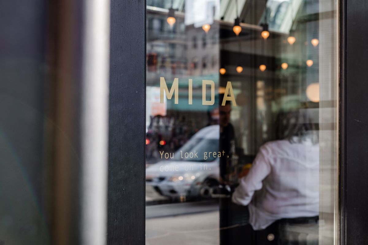 Closeup of a glass door that says, in all caps, “MIDA.” Underneath it are the words “you look great, come on in.”