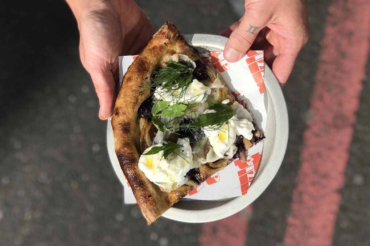 ASAP Pizza Borough Market shows off a slice of pizza with fragola grape, stracciatella, and fennel fronds held from a birdseye view over a road
