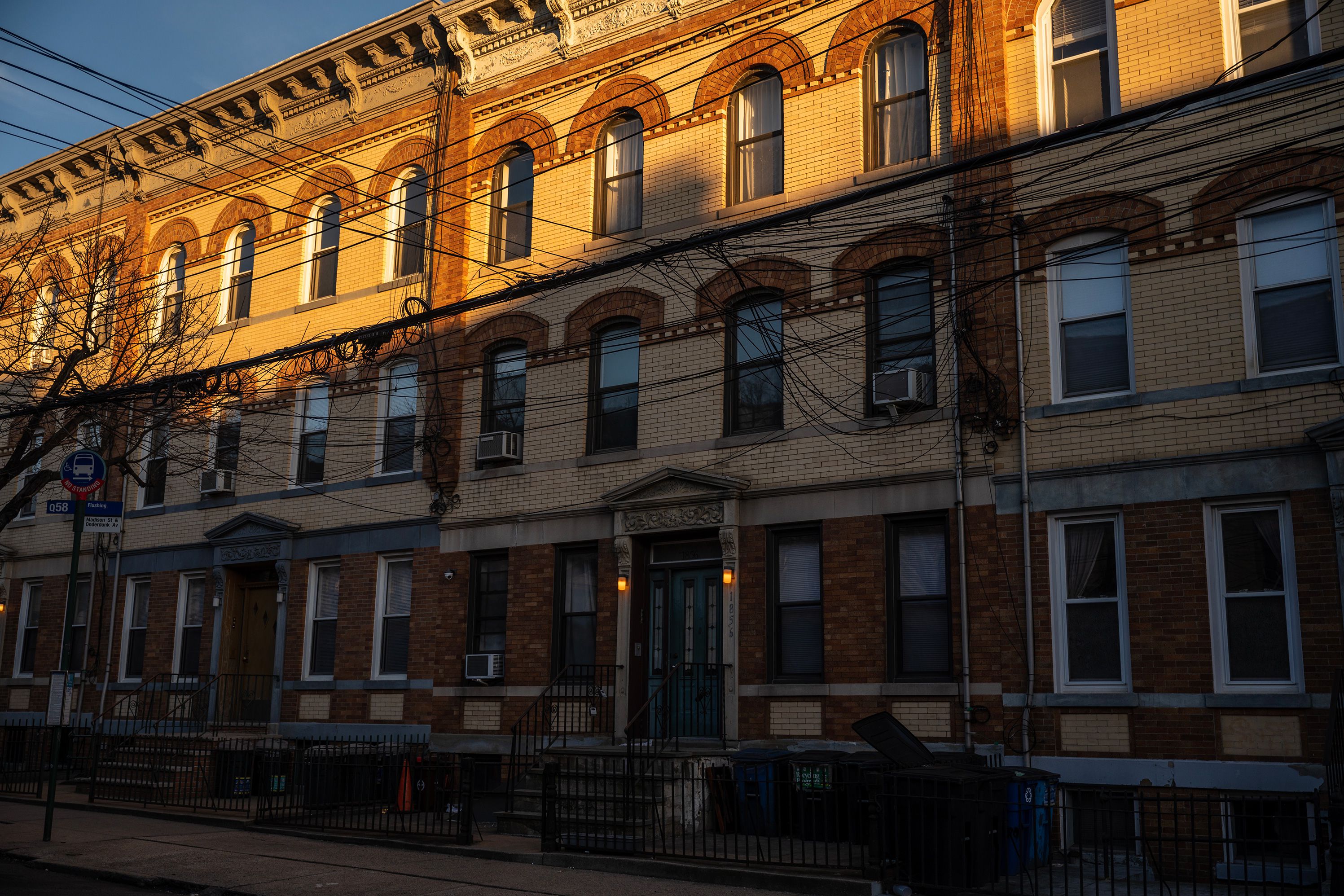 Golden sunset light illuminated the top floor of a row of tenement buildings on a Ridgewood residential block.