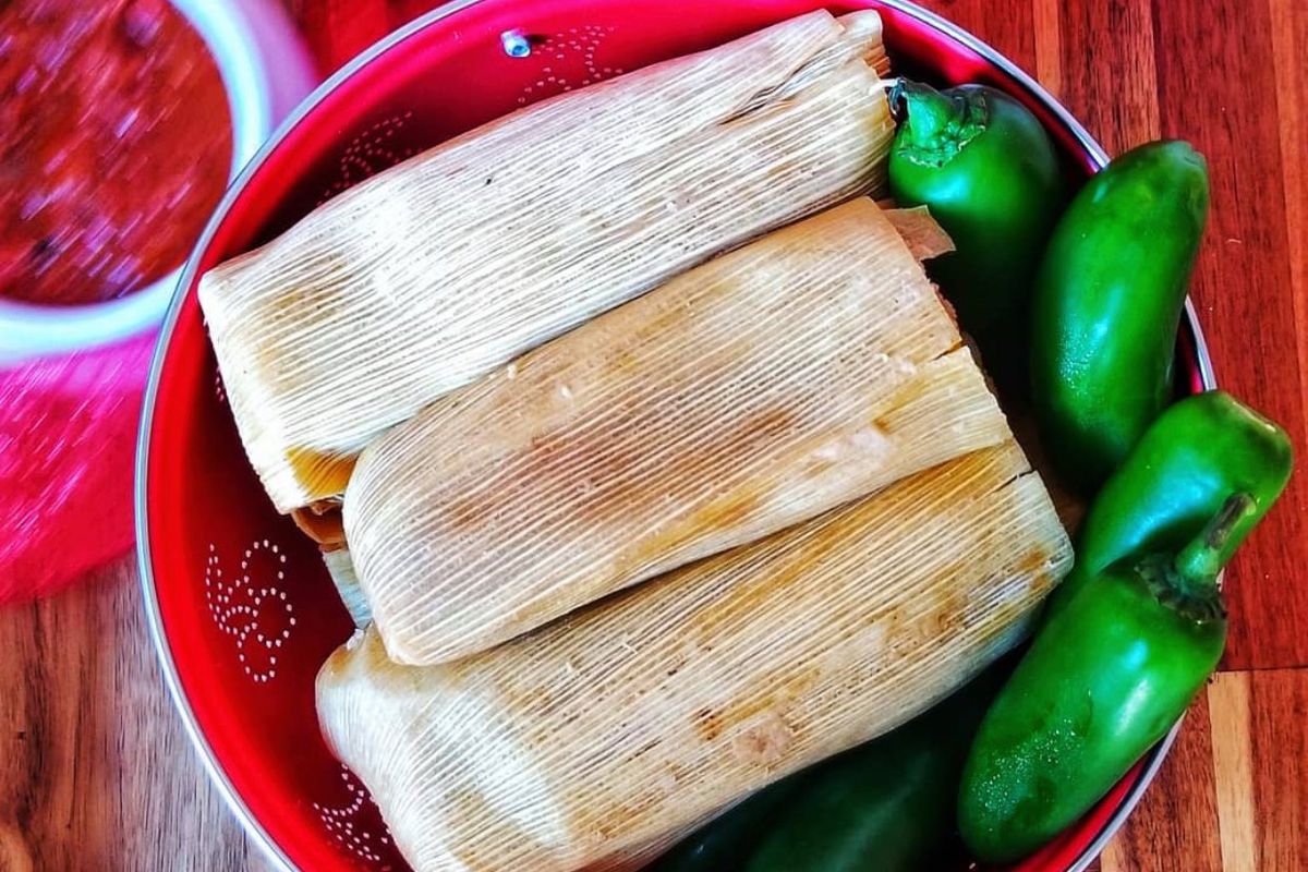 Three tamales in a red bowl with green peppers