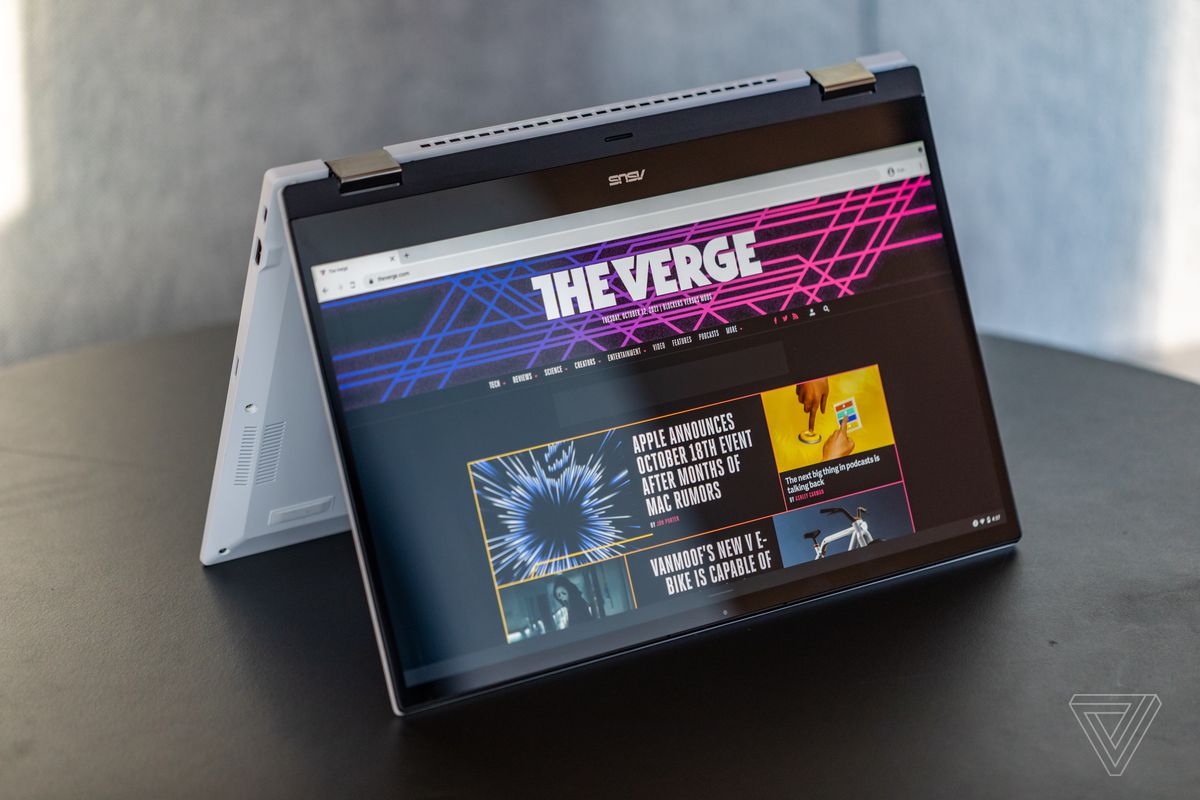 The Asus Chromebook Flip CX5 in tent mode, tilted to the left on a black table.  The screen displays the The Verge homepage.