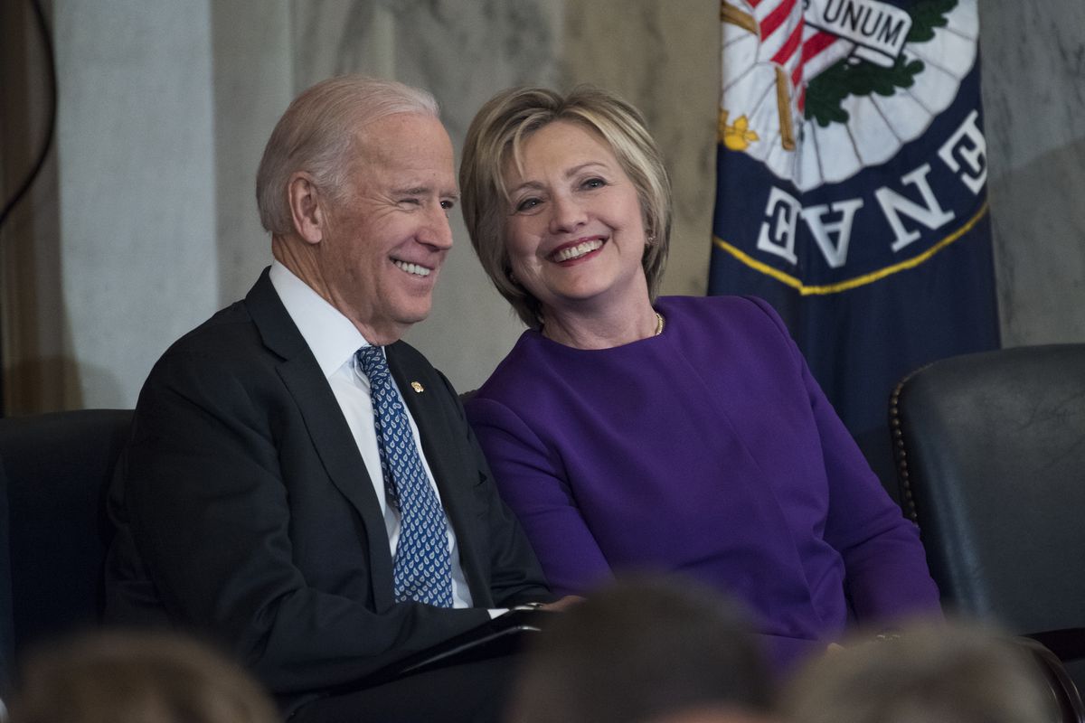 Joe Biden and Hillary Clinton sit and smile as they attend a ceremony in the Russell Building’s Kennedy Caucus Room, December 8, 2016.