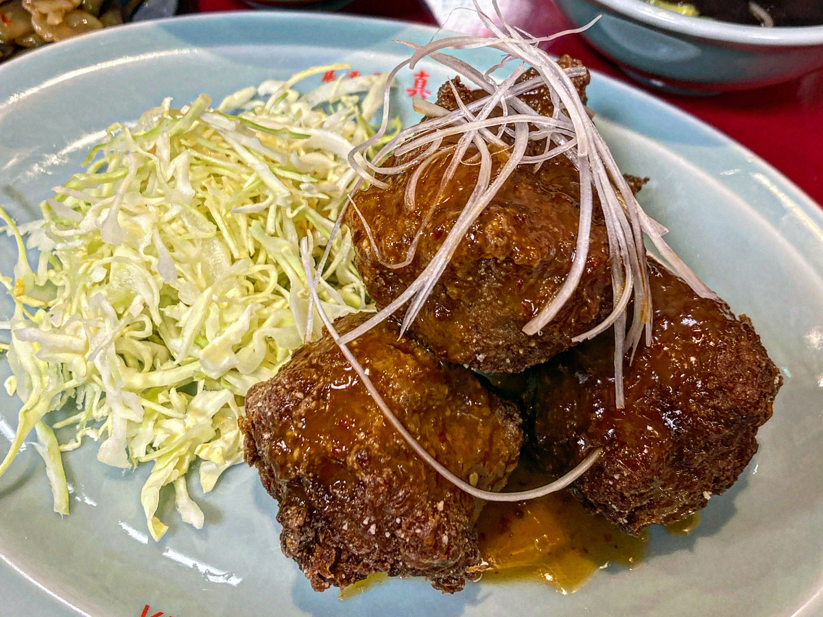 Three pieces of glossy glazed fried vegan karaage served with shredded cabbage and sides.