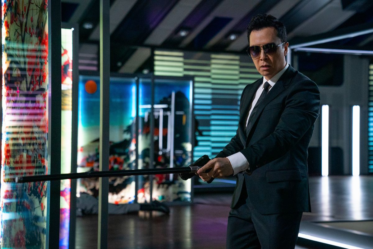 Donnie Yen, wearing a suit and sunglasses, holds out a gun and a can in John Wick: Chapter 4.