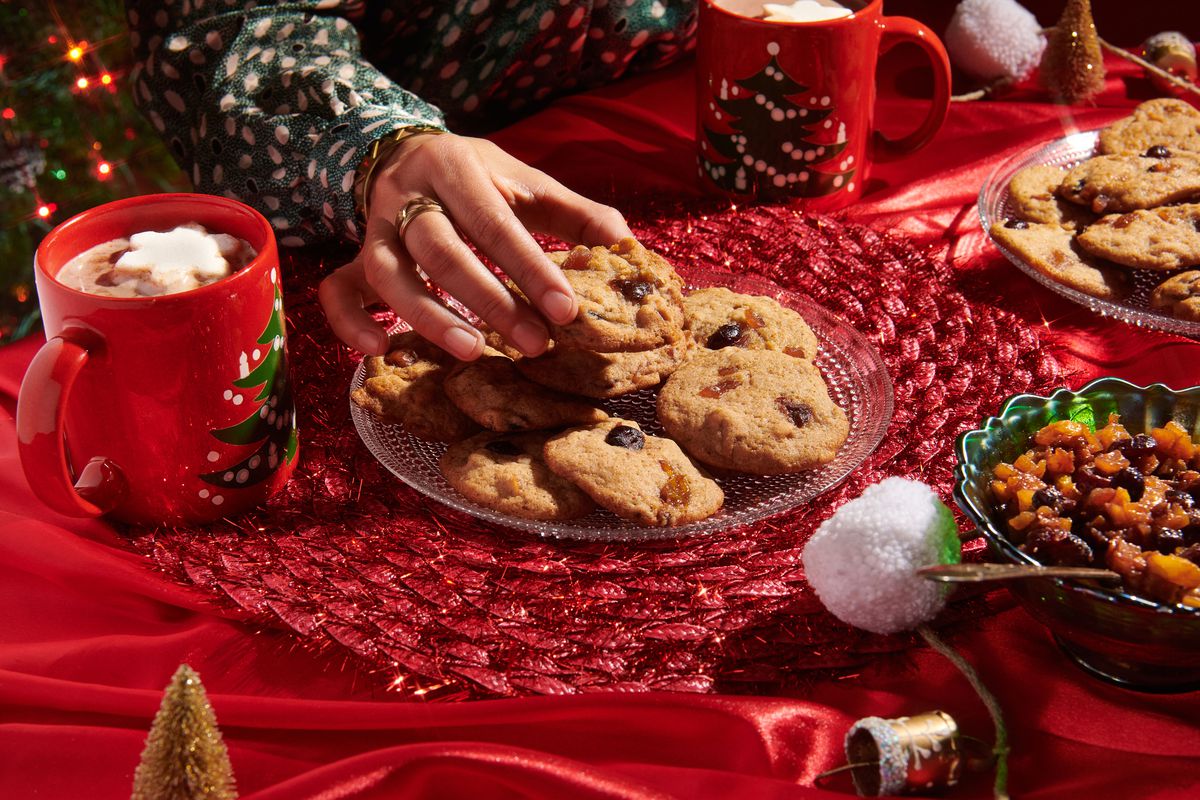 Hand reaches out to grab a mincemeat cookie from a pile of cookies on a table decorated for the holidays.