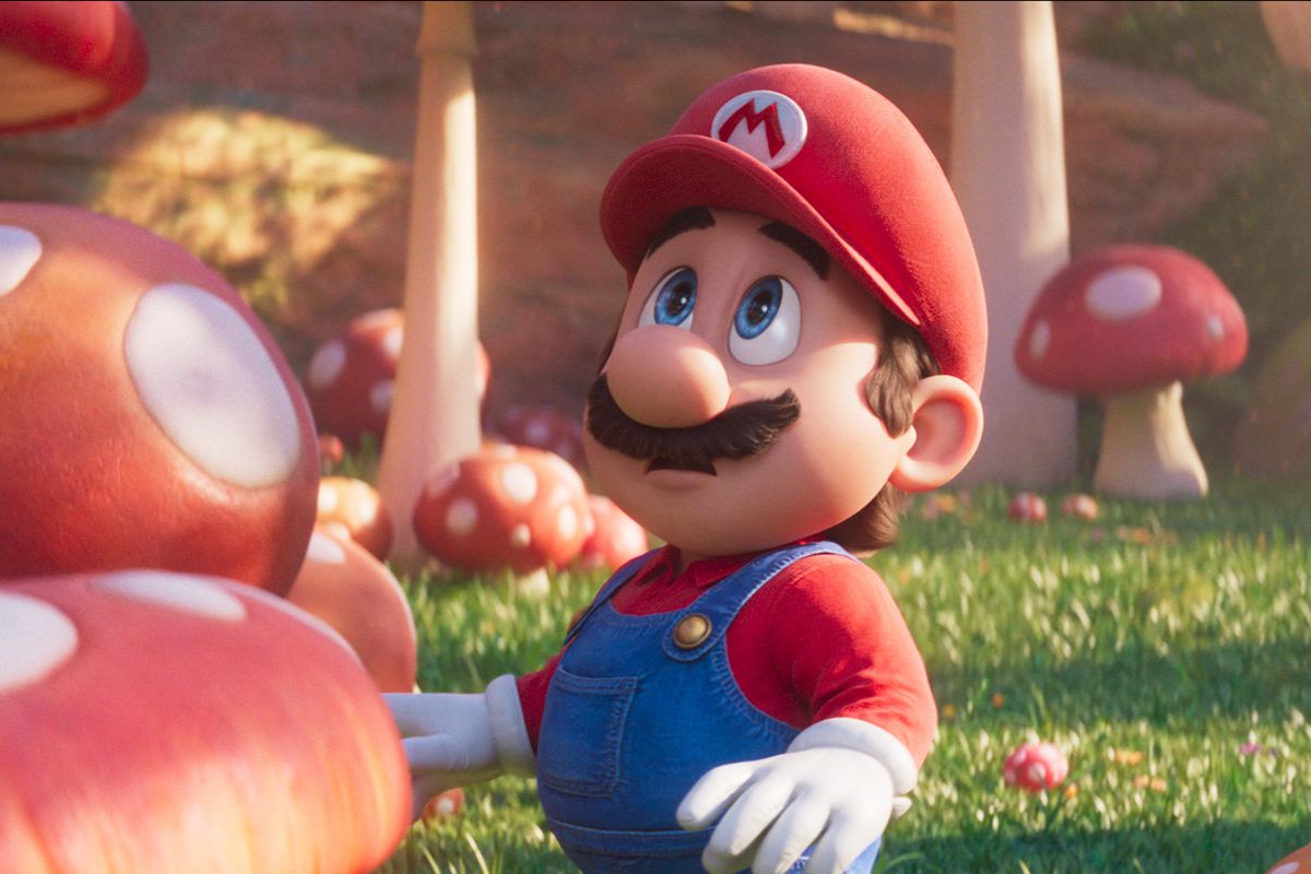 Mario looking up while he’s standing amid red mushrooms of various sizes in a field of grass in the Mushroom Kingdom,&nbsp;in the CG-animated Super Mario Bros. Movie