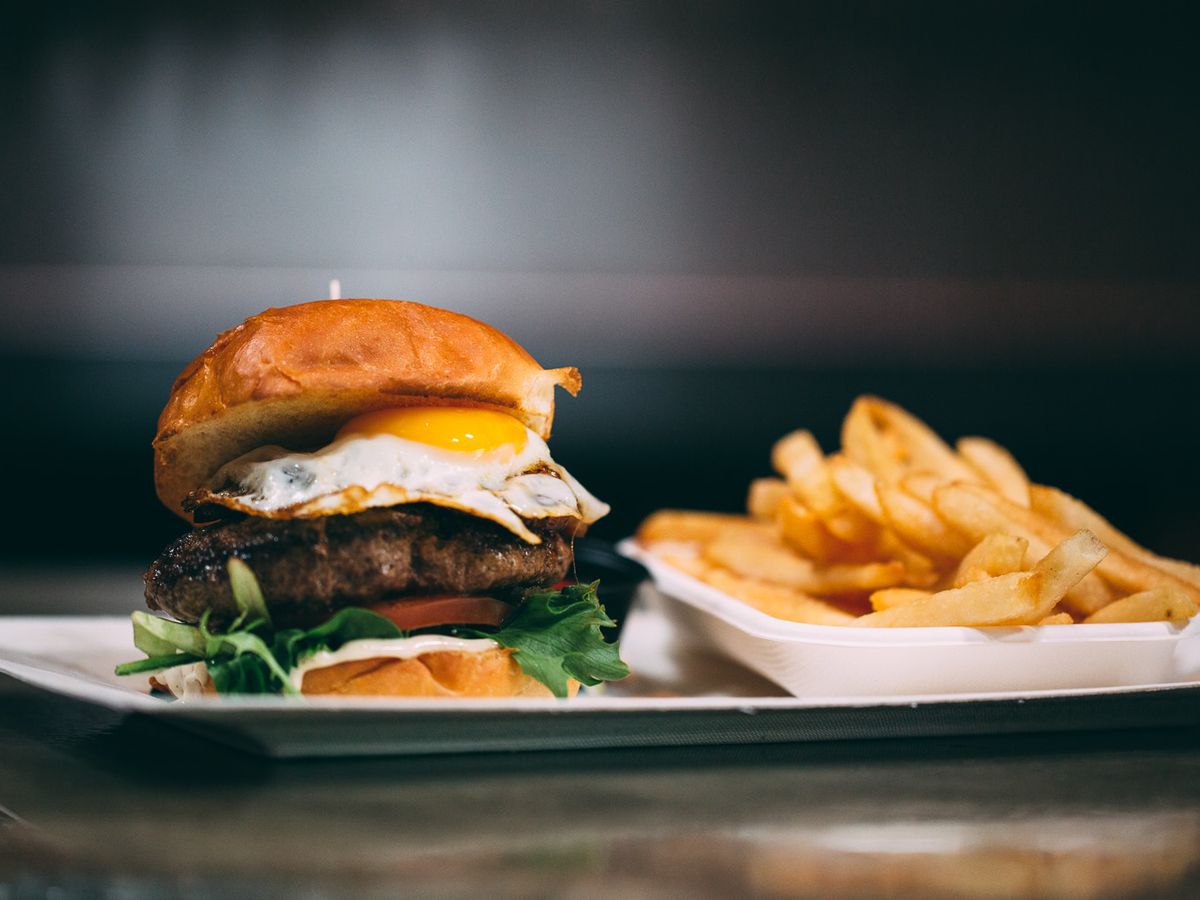 Burger topped with over easy egg next to pile of French fries.