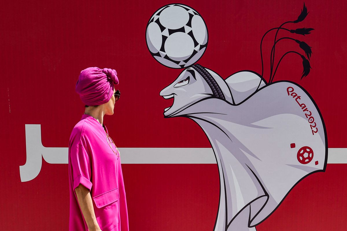 Bir kadın, 13 Ekim 2022'de Katar'ın başkenti Doha'daki West Bay'de Katar 2022 FIFA Dünya Kupası maskotu “La'eeb”i gösteren bir şantiye çitindeki bir illüstrasyona bakıyor.