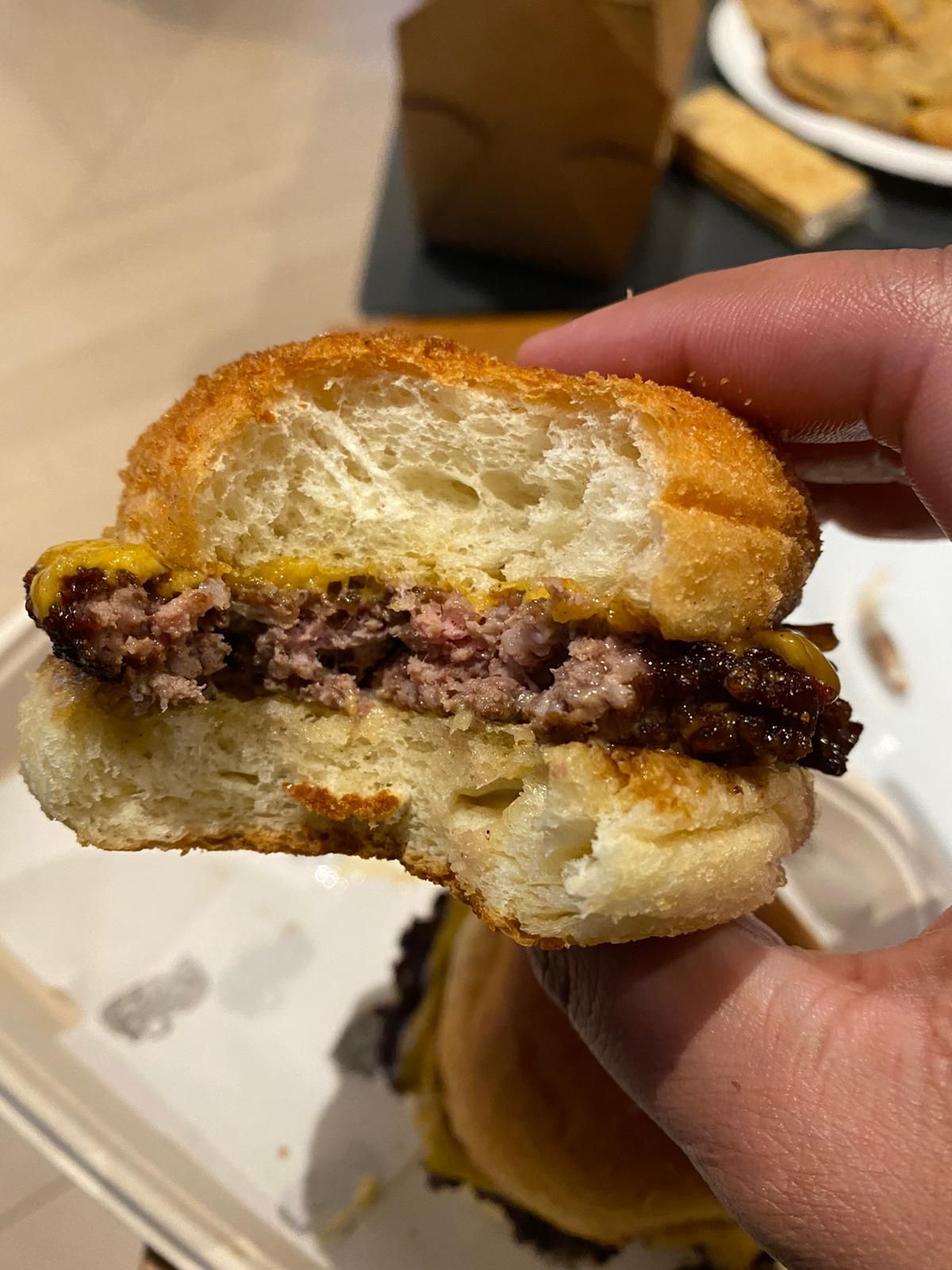 A cross-section of a slider with a bite taken out of it, with pandesal bun, beef burger, burnt onions, and cheese