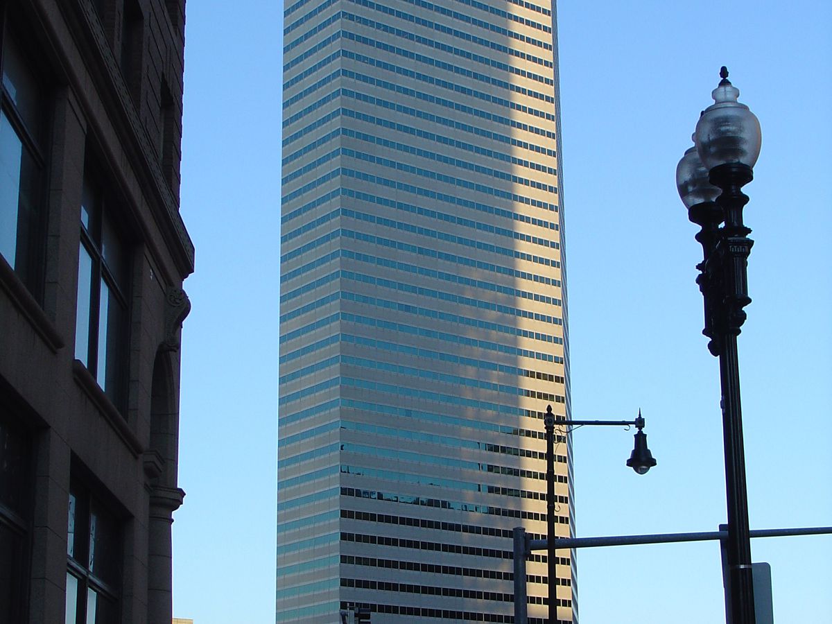 In the foreground is a street and a street lamp. In the distance is One Financial Center in Boston. The building is very tall with multiple windows.
